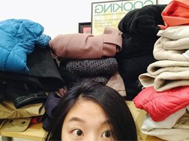 Half of our staff's head taking a selfie with all the folded donated coats!