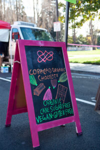 A black board stand with a pink frame, written on the board is "Coracao Organic Chocolate, organic, cane sugar free, vegan, gluten free"