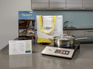a portable induction hob with a stainless steel pan, tote bag, and recipe cards on a kitchen counter