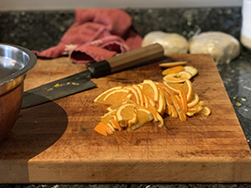 Thinly cut oranges with a knife on a wooden cutting board.