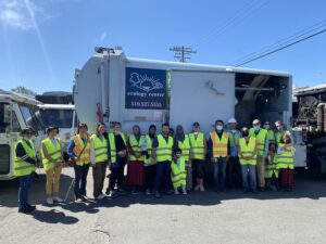 Image of Recycling Center Tour participants smiling in high visiability vests in front of an Ecology Center Recycling Truck.