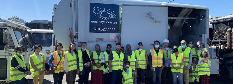 Image of Recycling Center Tour participants smiling in high visiability vests in front of an Ecology Center Recycling Truck.